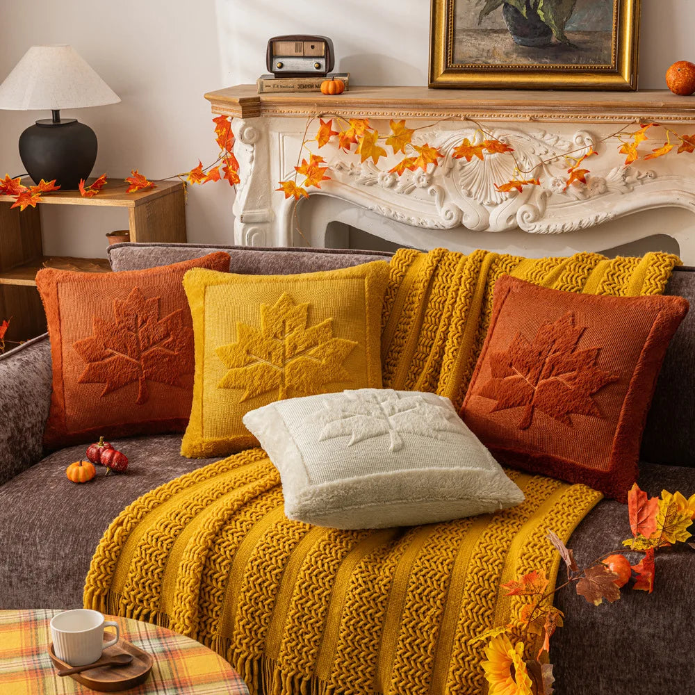 Maple leaf pillow covers in four colors on a sofa with a mustard throw