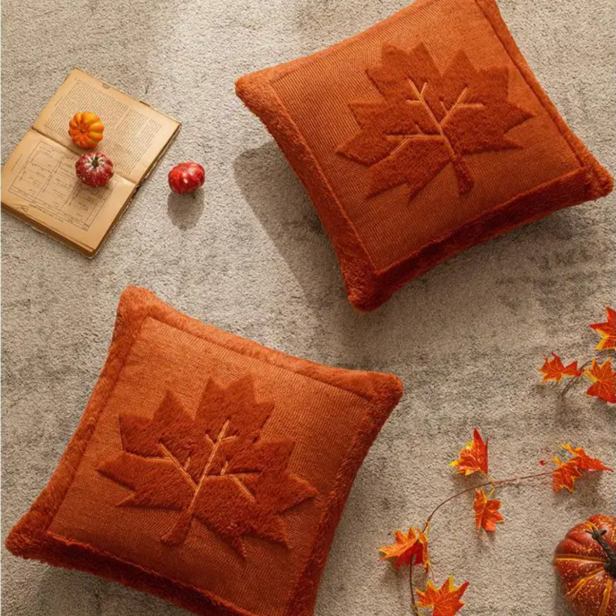Two maple leaf pillow covers laid flat with fall leaves