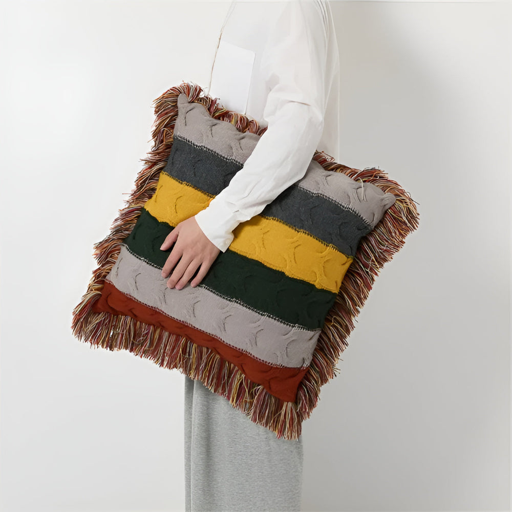 Striped cable knit cushion with fringe held under an arm
