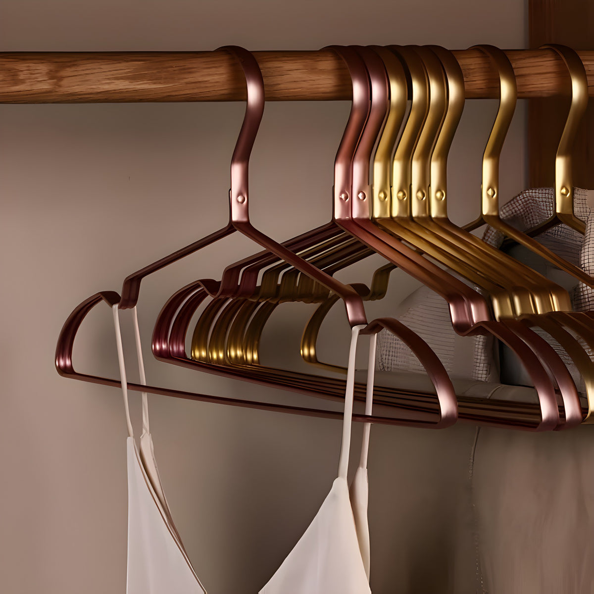 Rose pink and gold aluminum clothes hangers holding a silk camisole in a closet