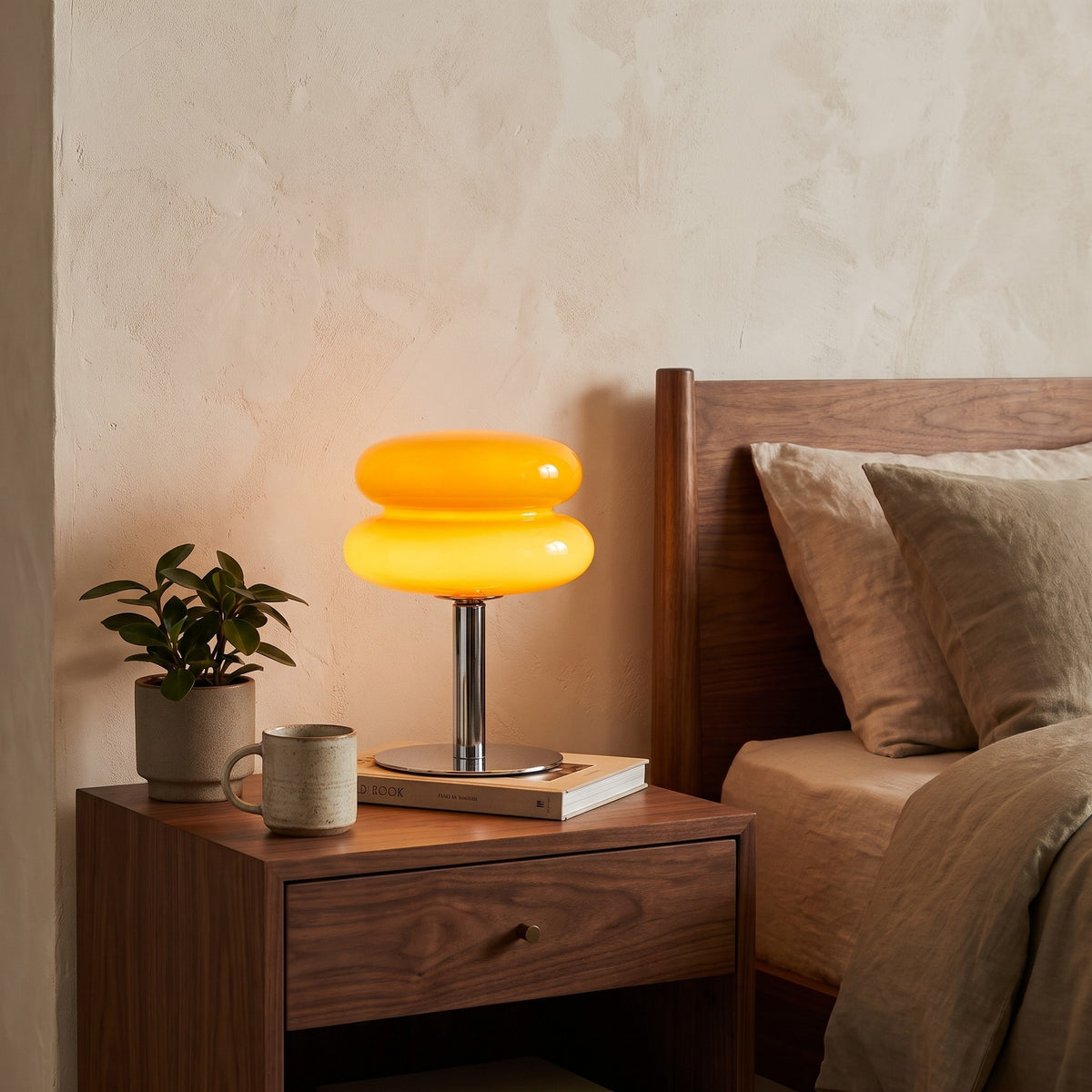 Annika glass table lamp in orange, lit on a walnut nightstand