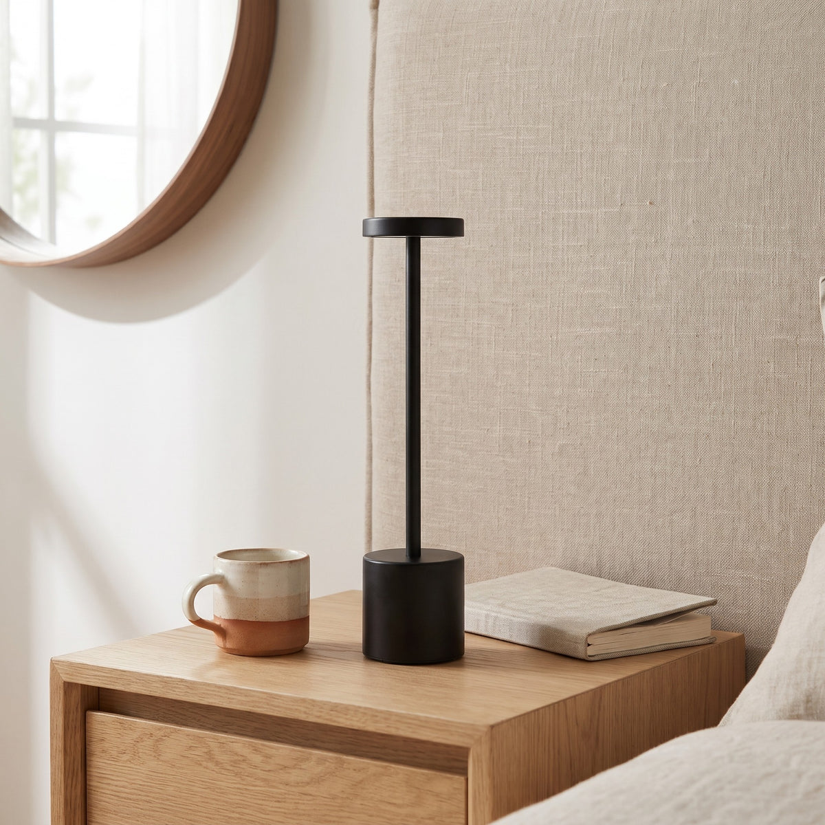 Black Asta cordless table lamp on a bedside table beside a mug