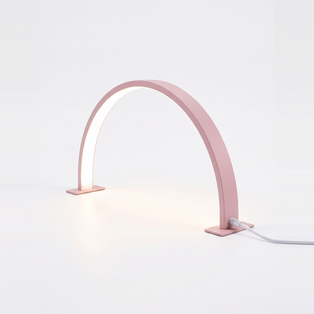 Pink half moon desk lamp lit on a white background