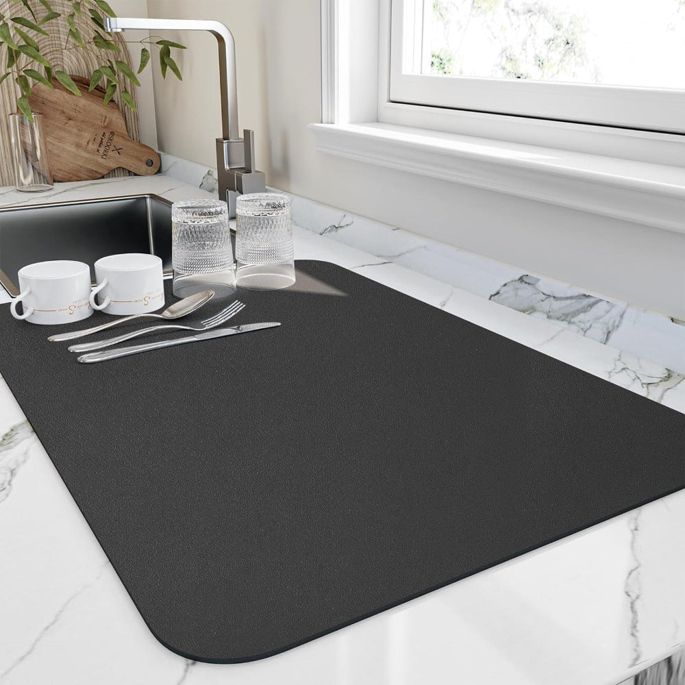 Black dish drying mat with cups and cutlery by a sink