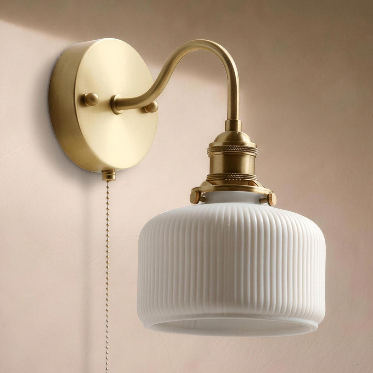 Fia wall sconce with a ribbed white ceramic shade and curved brass arm on a warm plaster wall