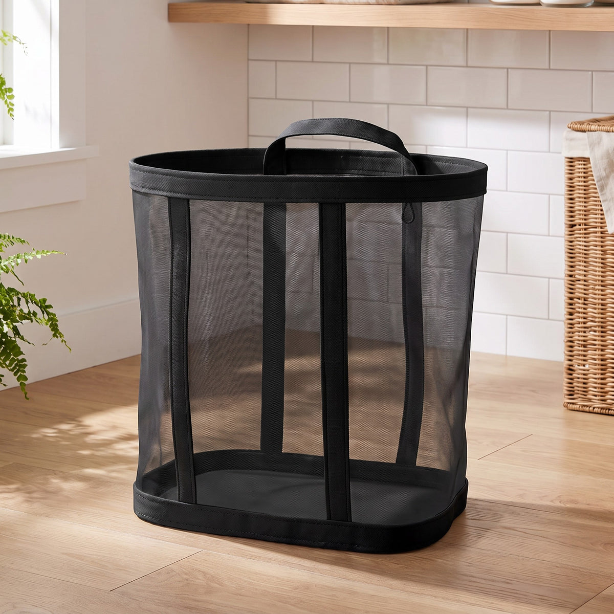 Black mesh laundry basket standing on a wood floor in a laundry room