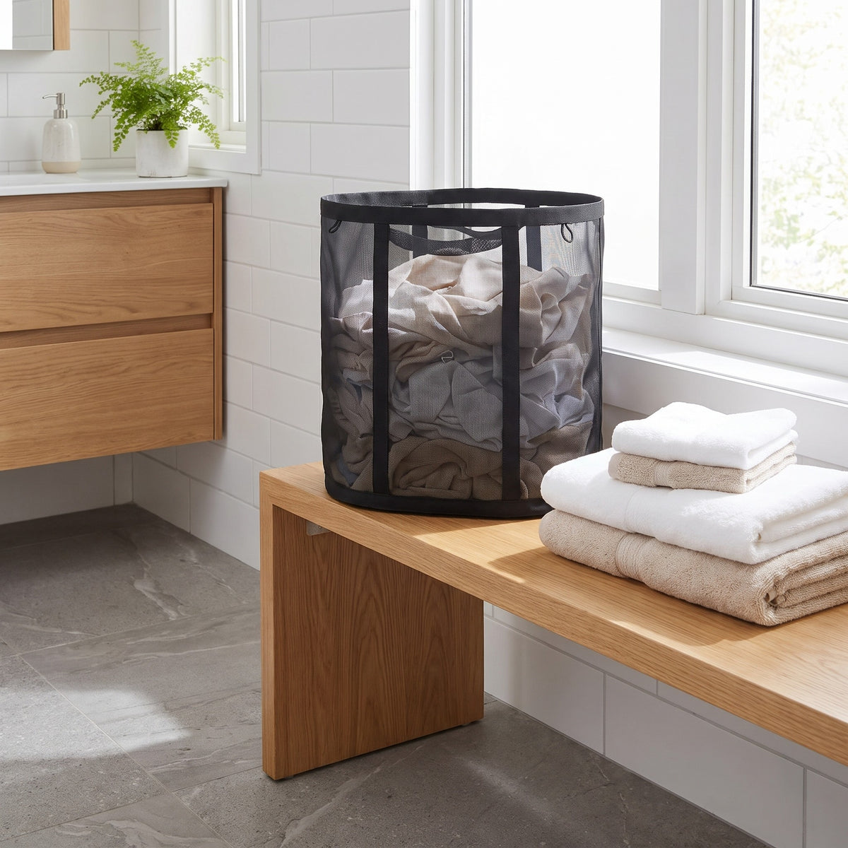 Black mesh laundry basket full of towels on a bathroom bench