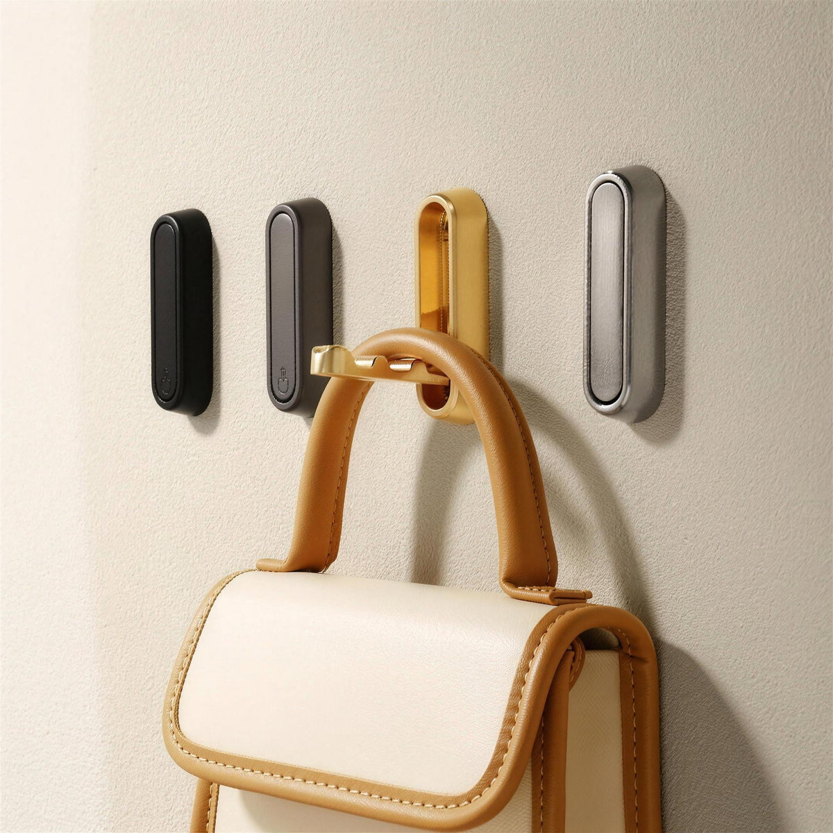 Folding wall hooks in four finishes on a wall, one holding a handbag