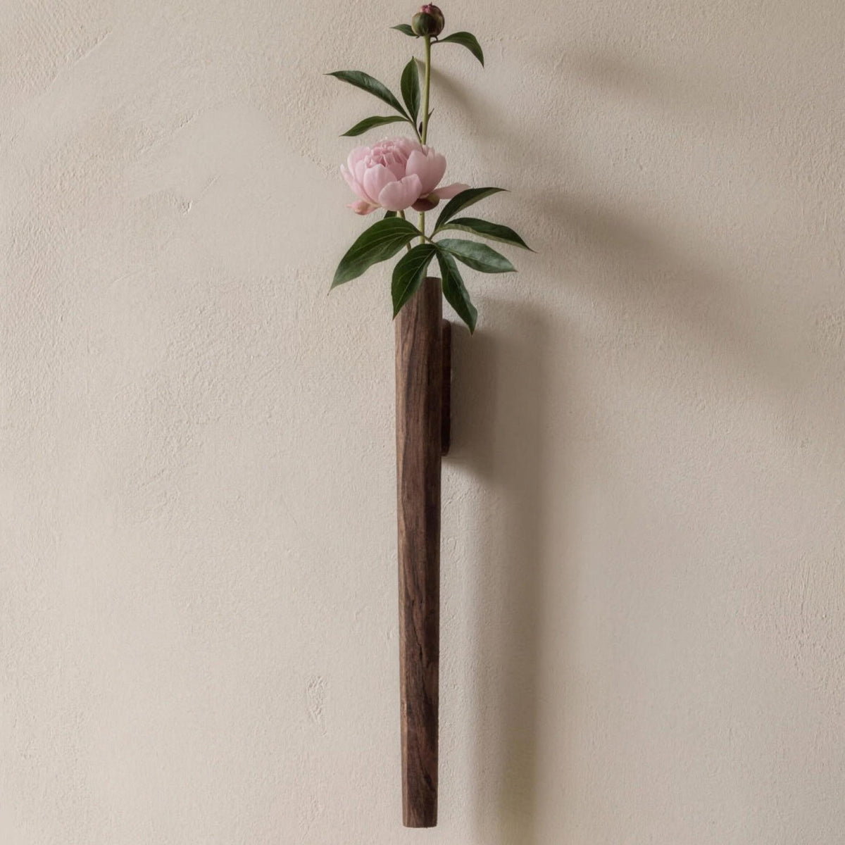 Idun black walnut wall vase holding a peony above a console table