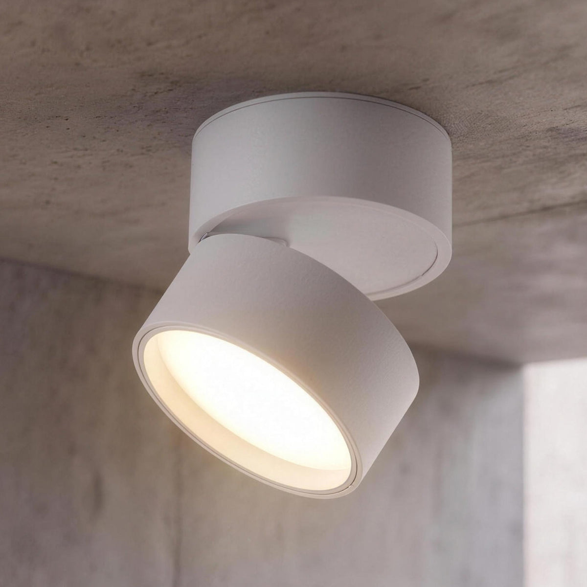 Ilse LED ceiling spotlight, white, head tilted and lit on a concrete ceiling
