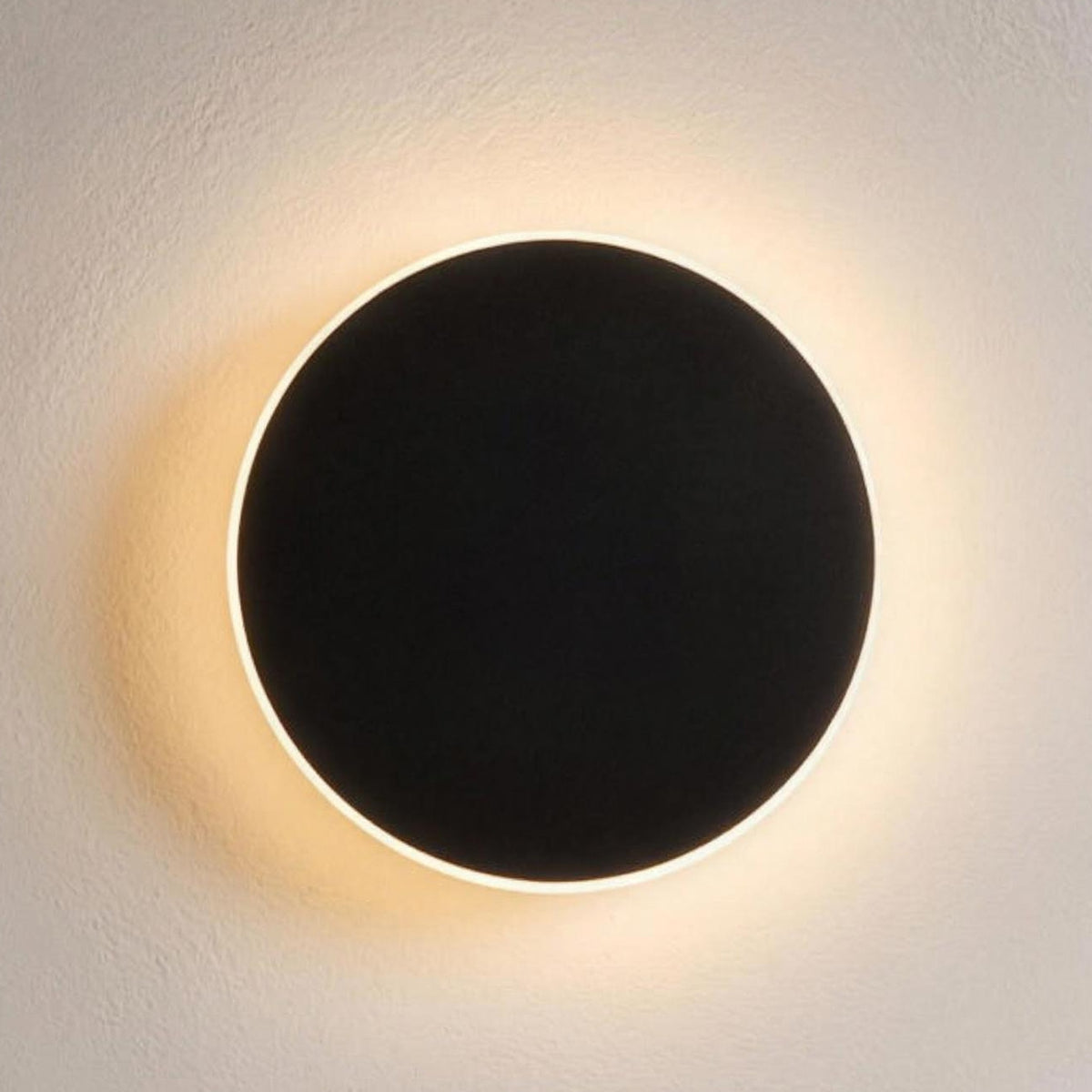 Kaja LED wall sconce, black disc with a warm halo on a plaster wall