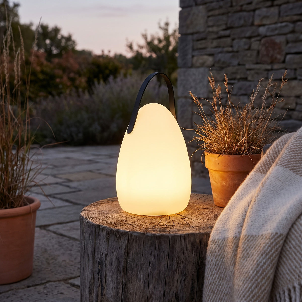 Teardrop Kari cordless lamp glowing on a log stool on a patio at dusk