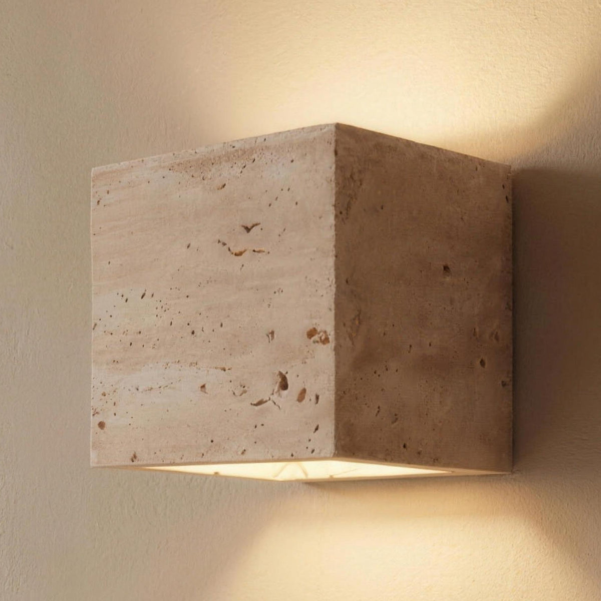 Square Karin travertine wall light lit on a plaster wall