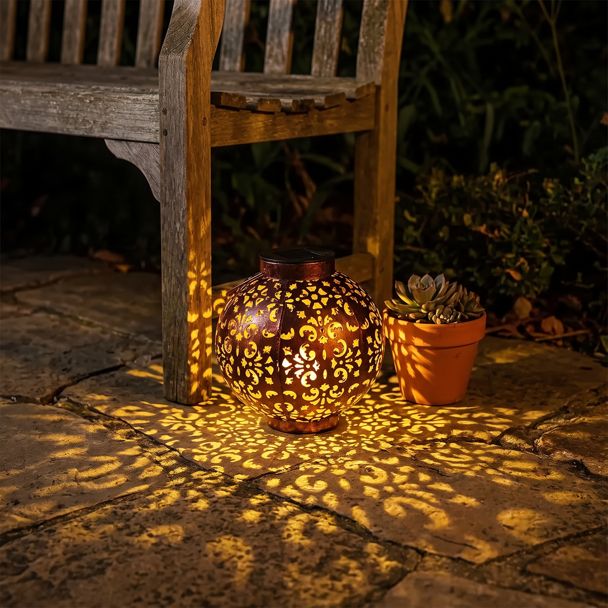 Mette solar lantern beside a garden bench, its pattern spread over the flagstones
