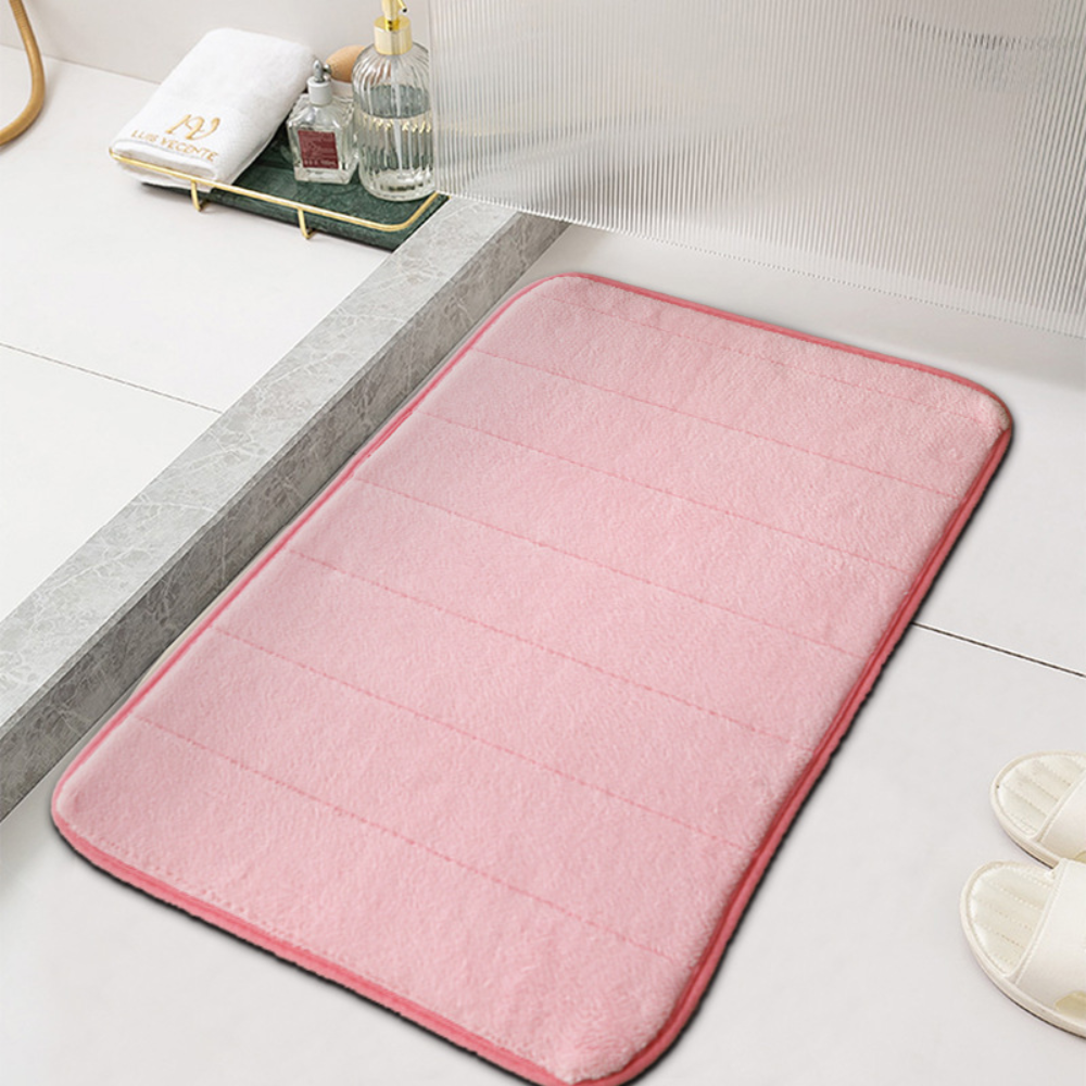 Pink microfiber bath mat with ribbed channels beside a white bathtub