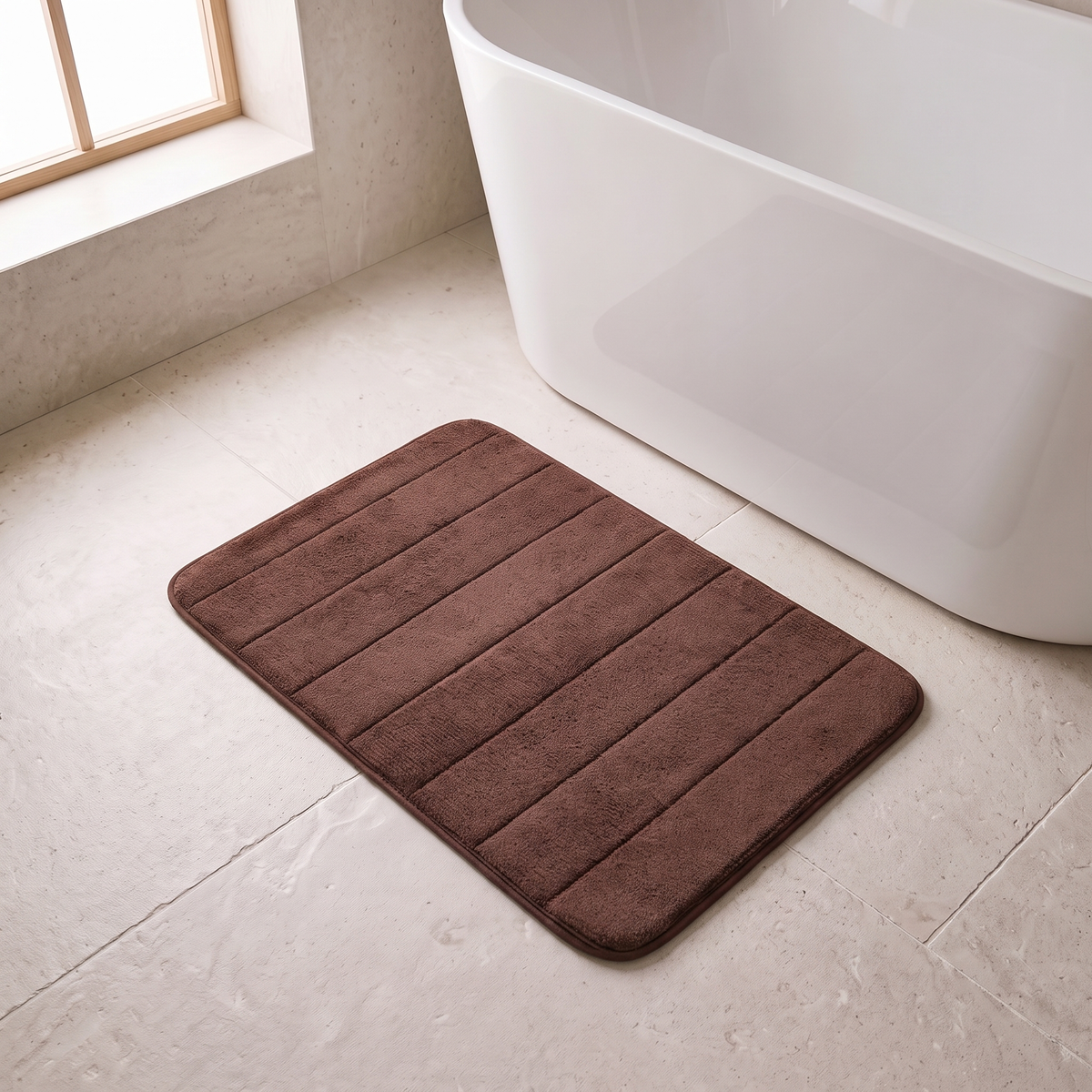 Microfiber bath mat in brown on a stone floor beside a bathtub