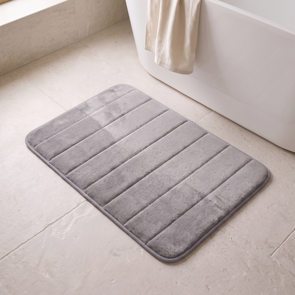 Microfiber bath mat in gray on a stone floor beside a bathtub