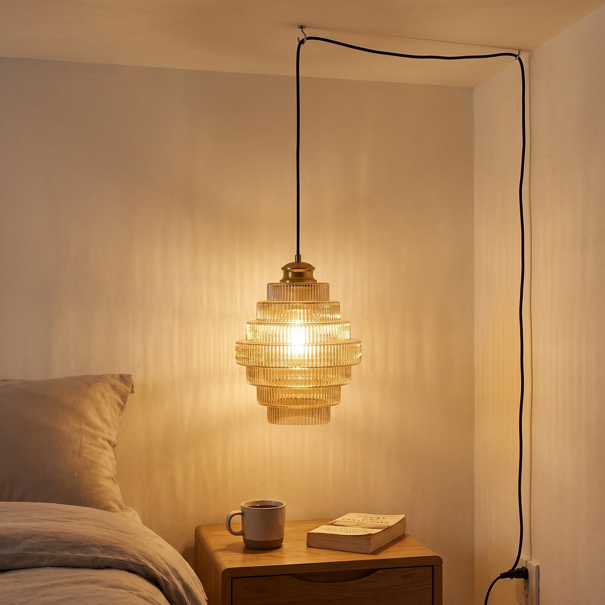 Minna pendant light in amber hanging low over a nightstand beside the bed, its cord running down to an outlet