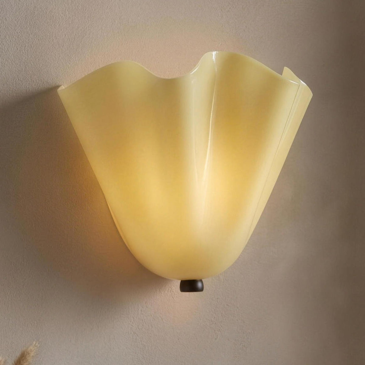 Moa wall sconce, beige ruffled glass shell, lit on a plaster wall