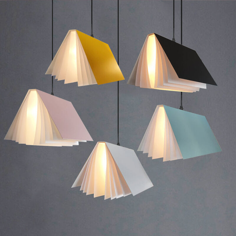 All five book pendant lights lit against a gray wall: yellow, black, pink, blue and white