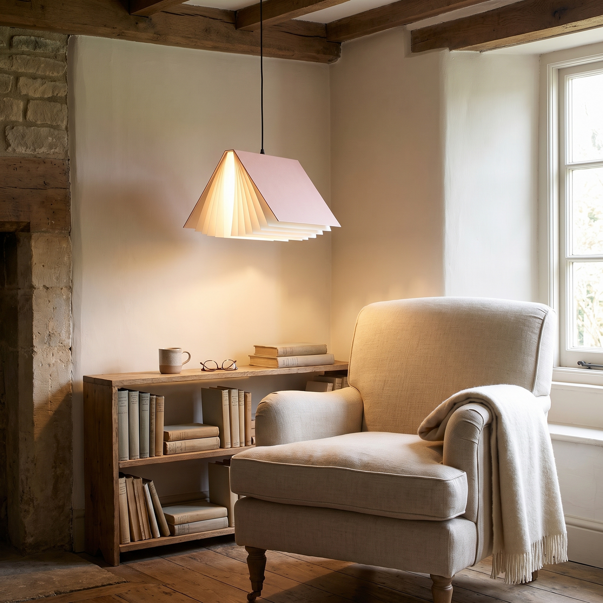 Pink book pendant light hanging over a linen armchair in a reading corner beside a low bookshelf