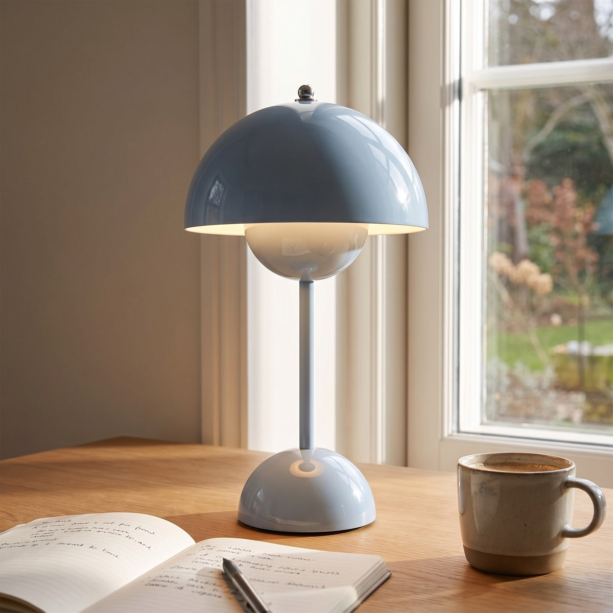 Oona table lamp in light blue on a desk beside an open notebook