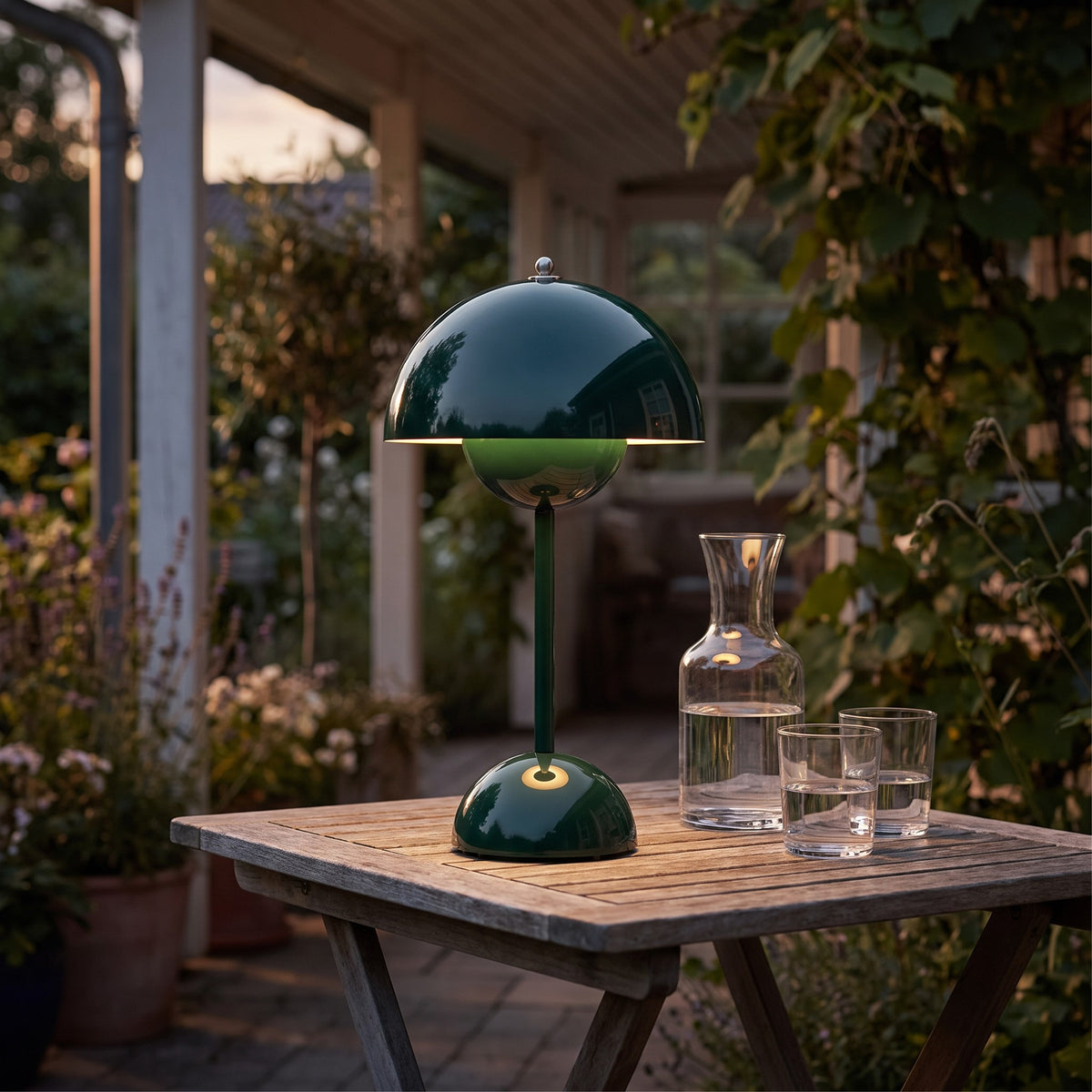 Oona table lamp in dark green on a covered patio table at dusk