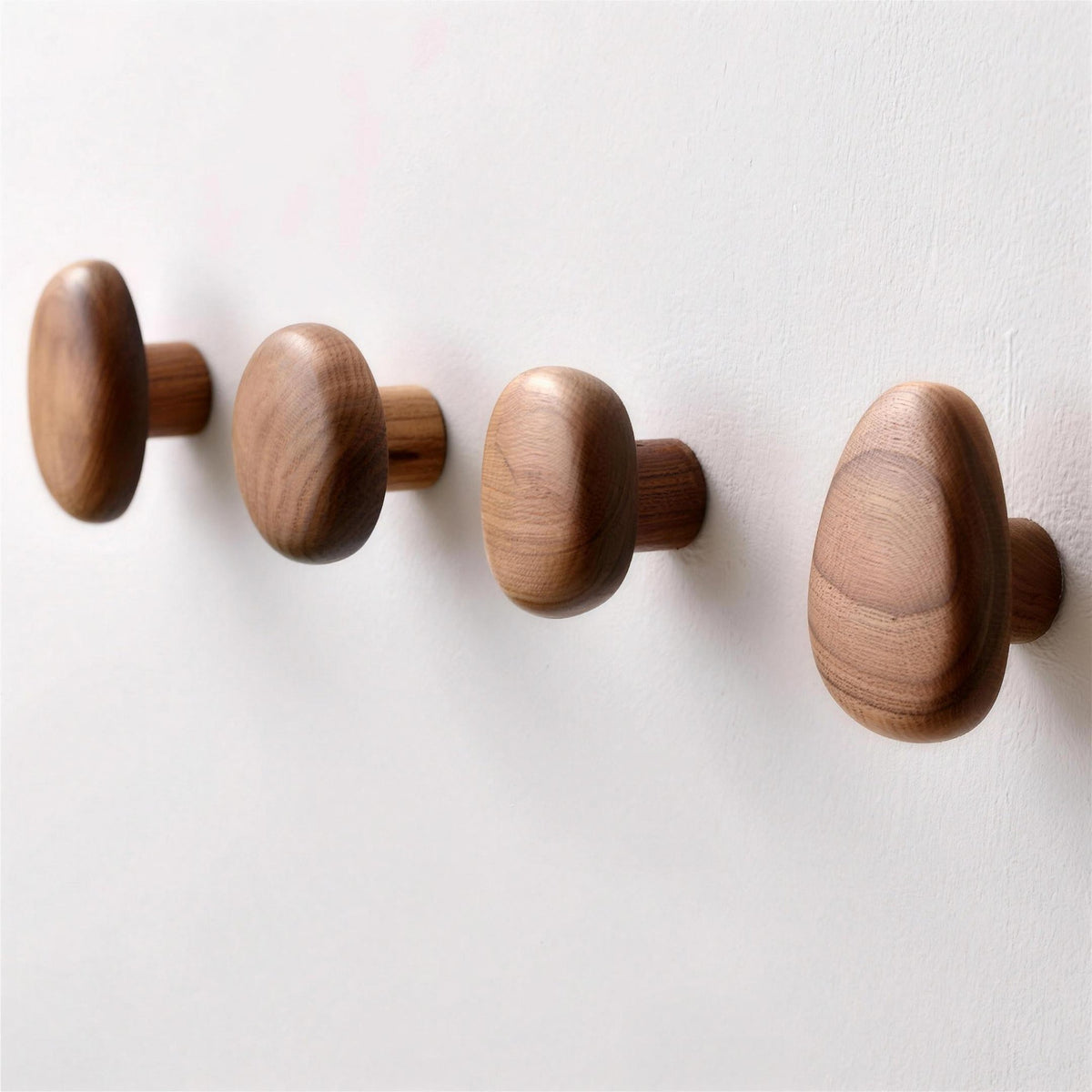 Walnut pebble wall hooks, set of four, on a plain wall