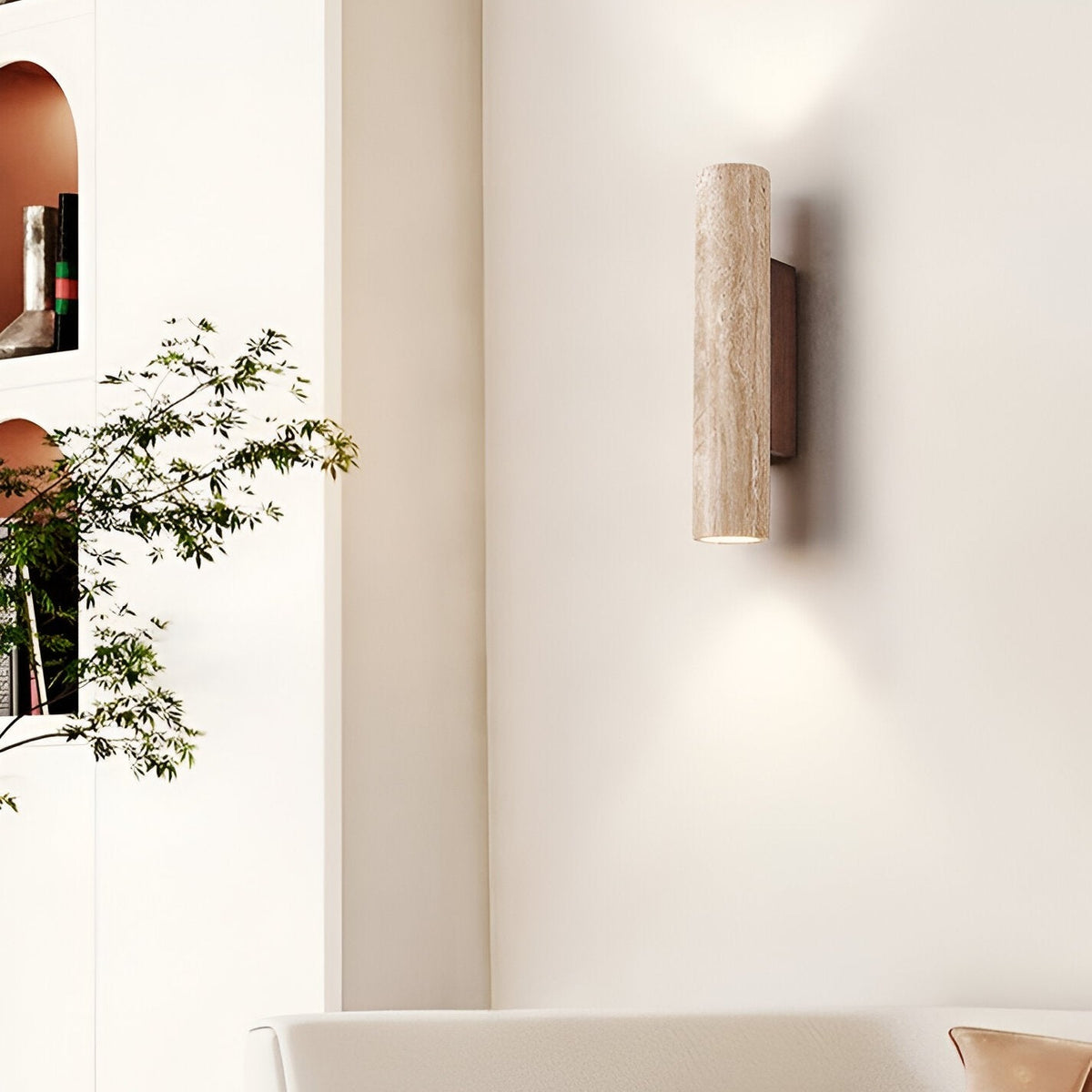 Rakel travertine wall sconce lit on a living room wall beside a potted plant