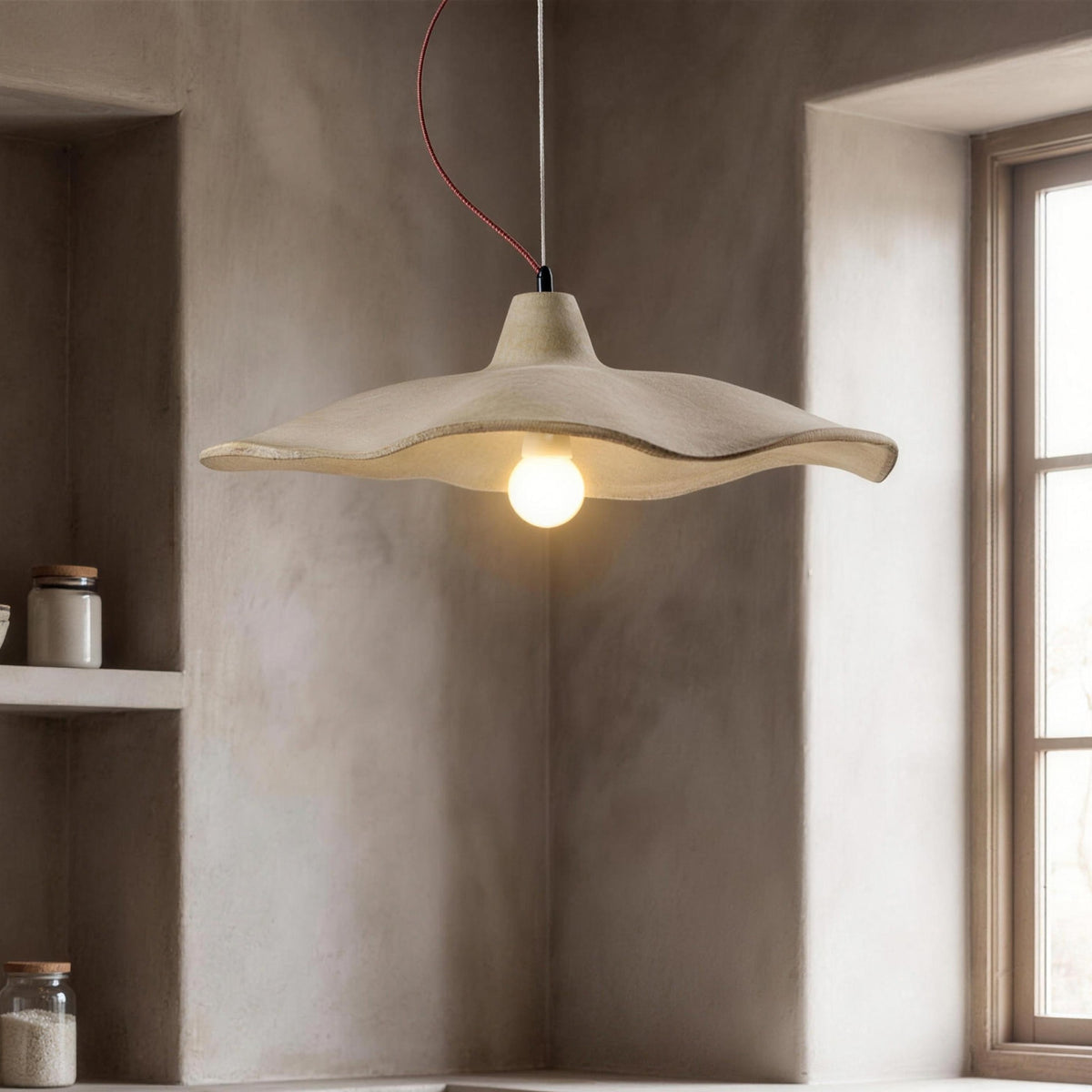 Sanna pendant light with wavy cement shade, lit against a gray plaster wall