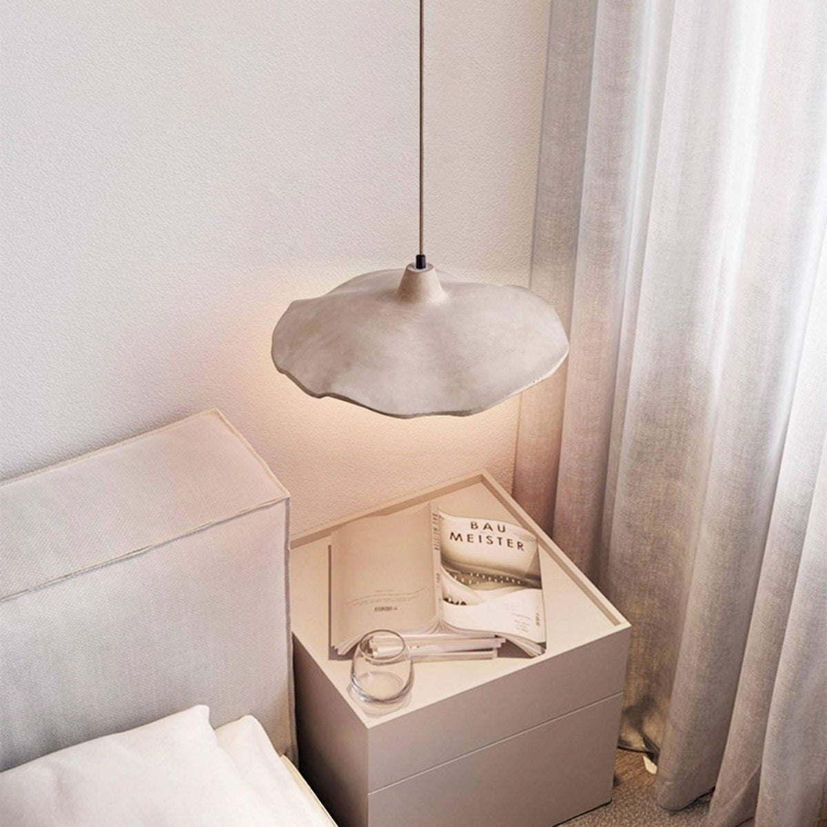 Sanna pendant light with wavy cement shade hung low beside a bed