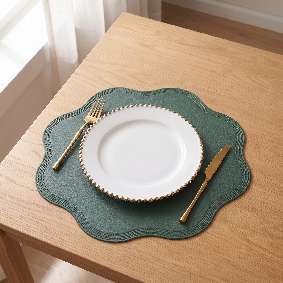 Scalloped placemat in green with a white plate and gold cutlery on an oak table