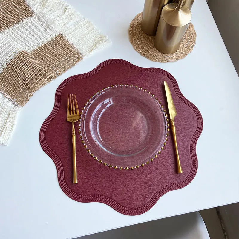 Red scalloped placemat with a glass plate and gold cutlery from above