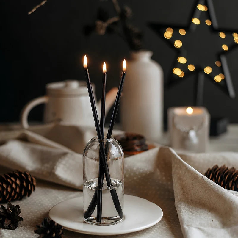 Skive black oil candles lit on a white plate with pinecones