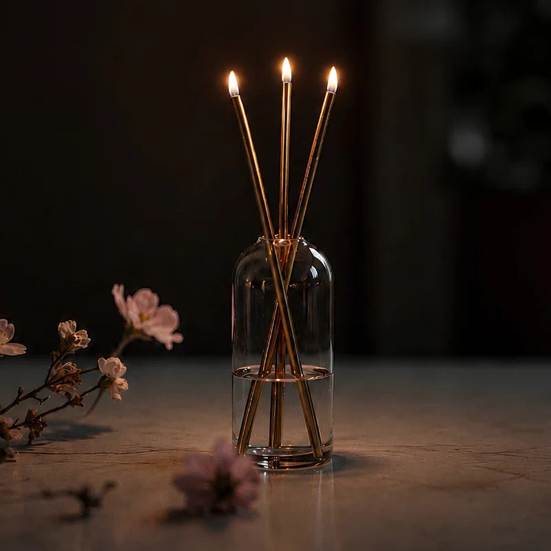 Skive gold oil candles lit on a dark table with blossoms
