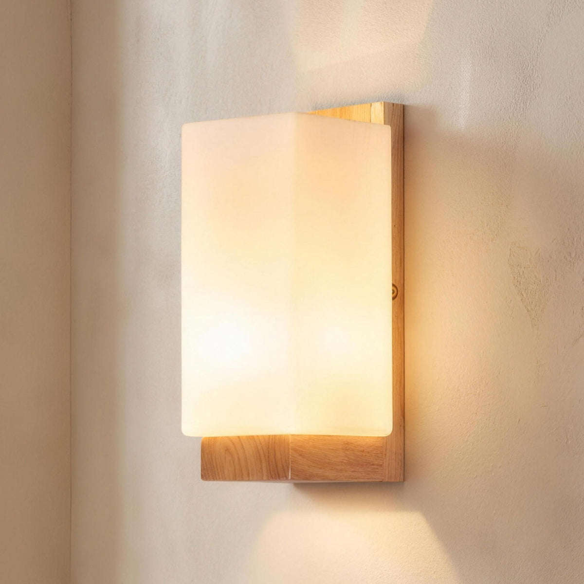 Sofie wall sconce, white glass shade on a natural wood plate, lit on a plaster wall