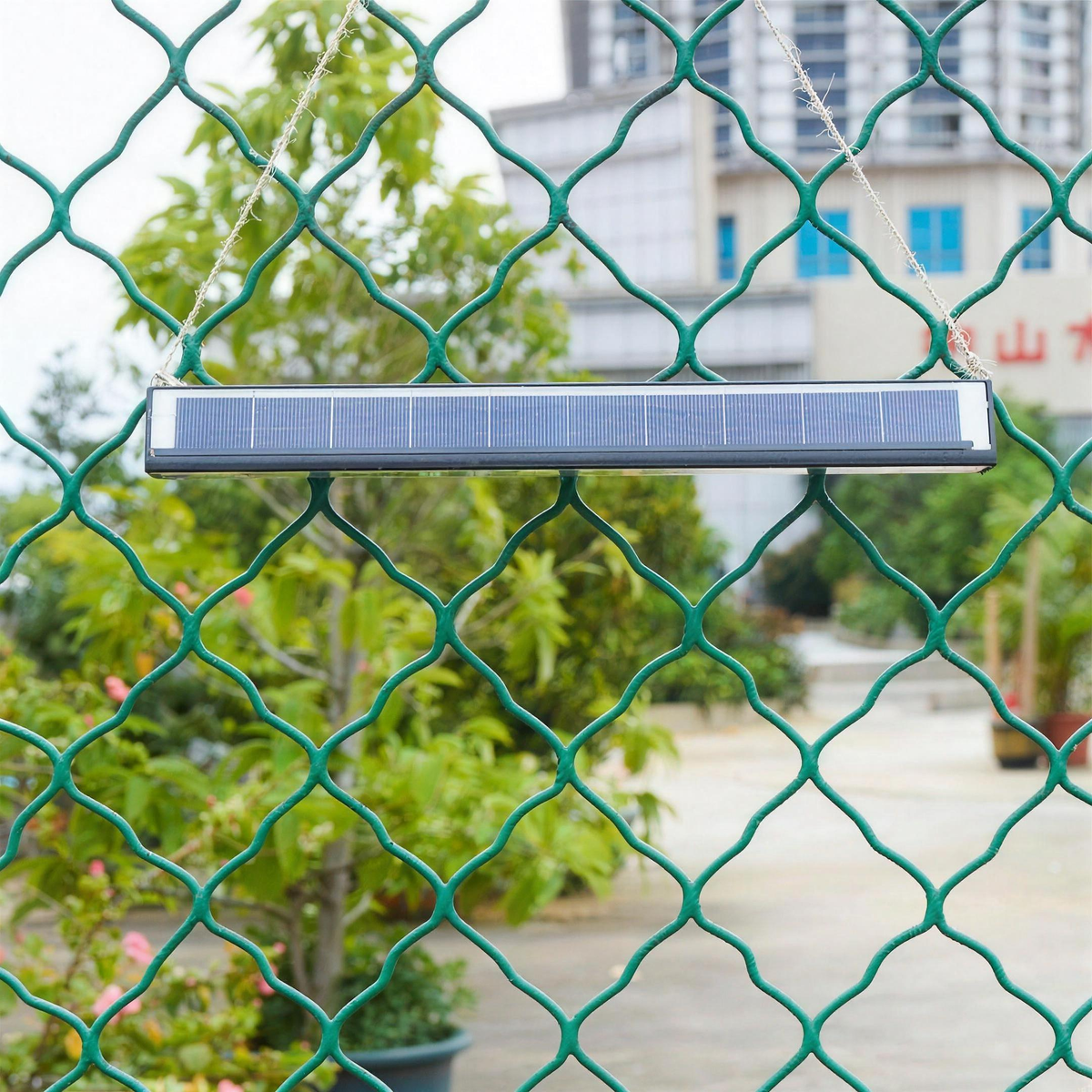 Solar wall light hung from a cord on a chain link fence