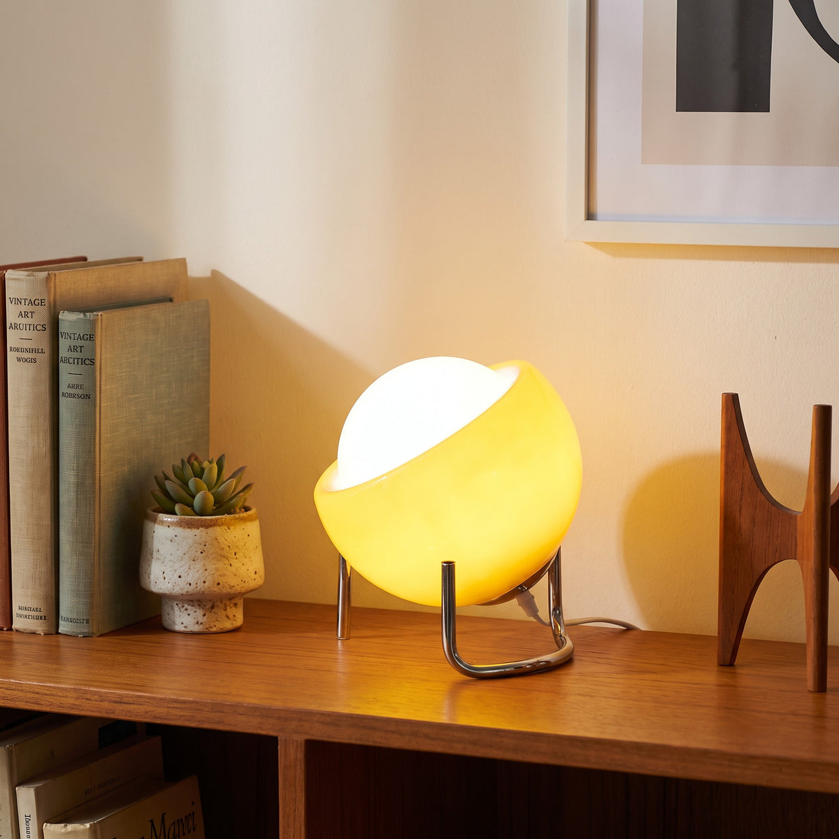 Solveig table lamp glowing on a teak bookshelf beside a small succulent