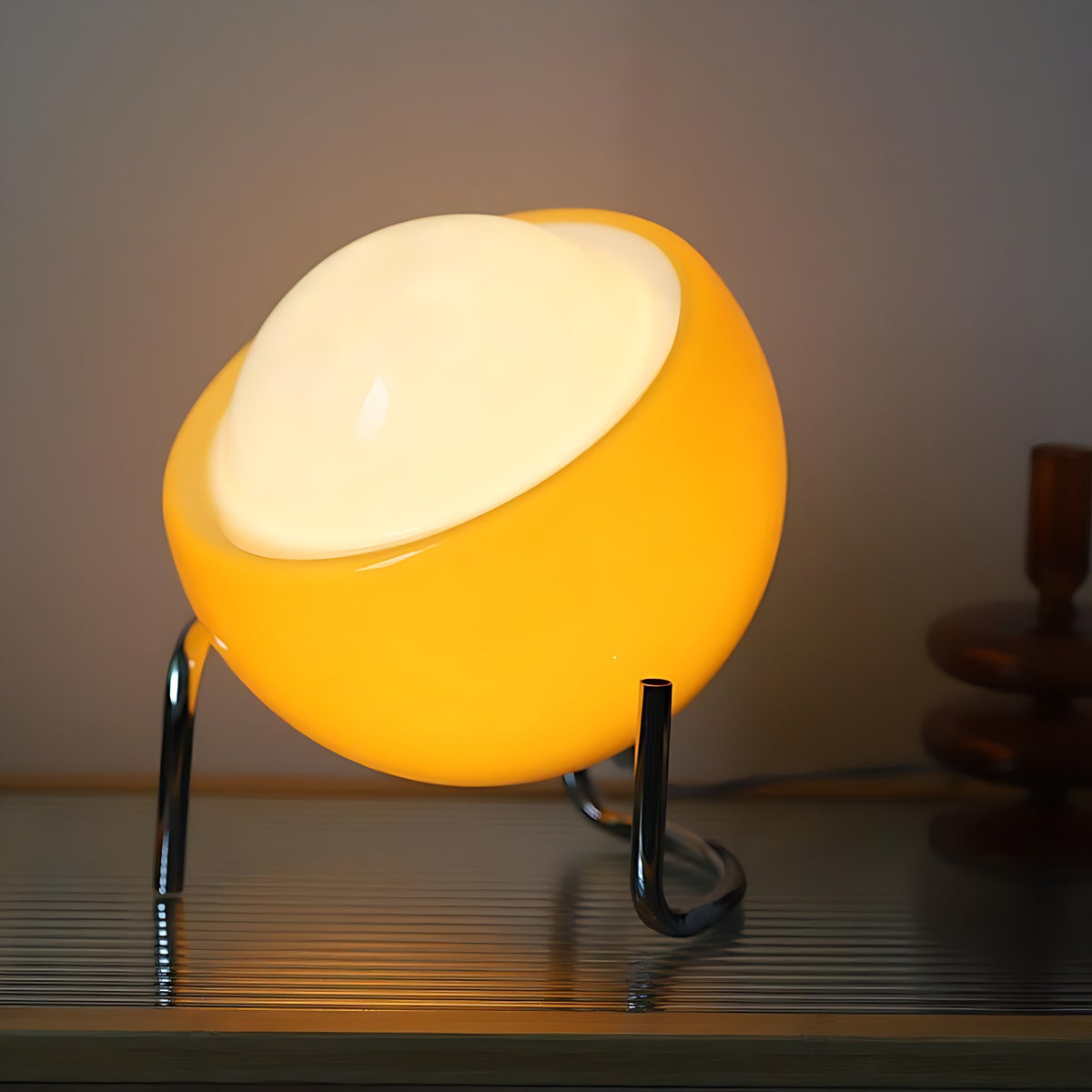 Solveig table lamp lit on a glass shelf beside an amber candle holder