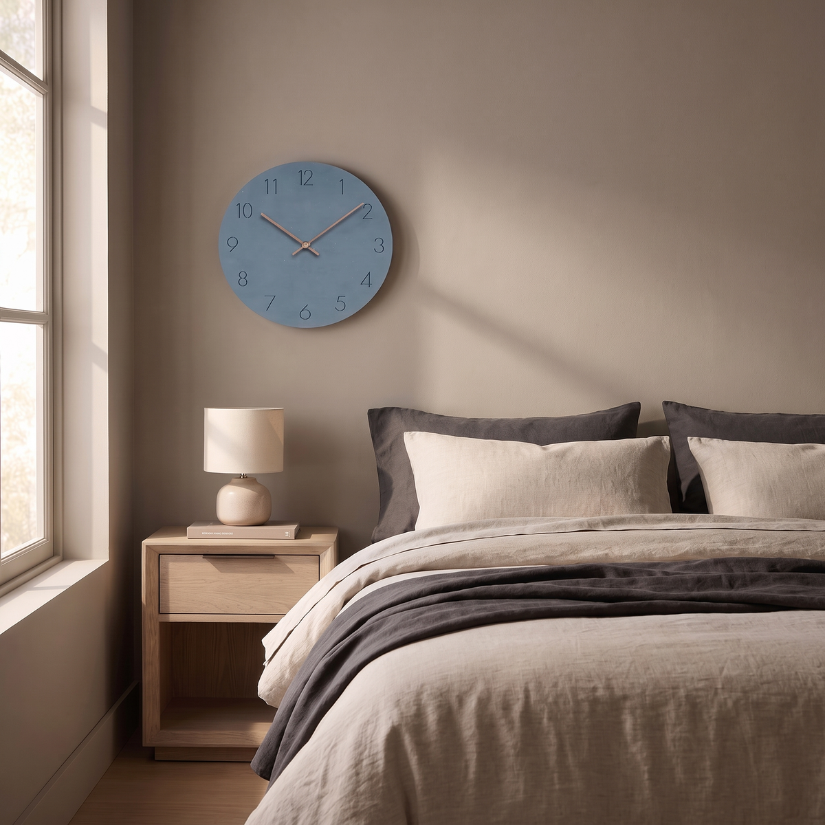 Slate blue wall clock above a nightstand next to a bed with linen bedding
