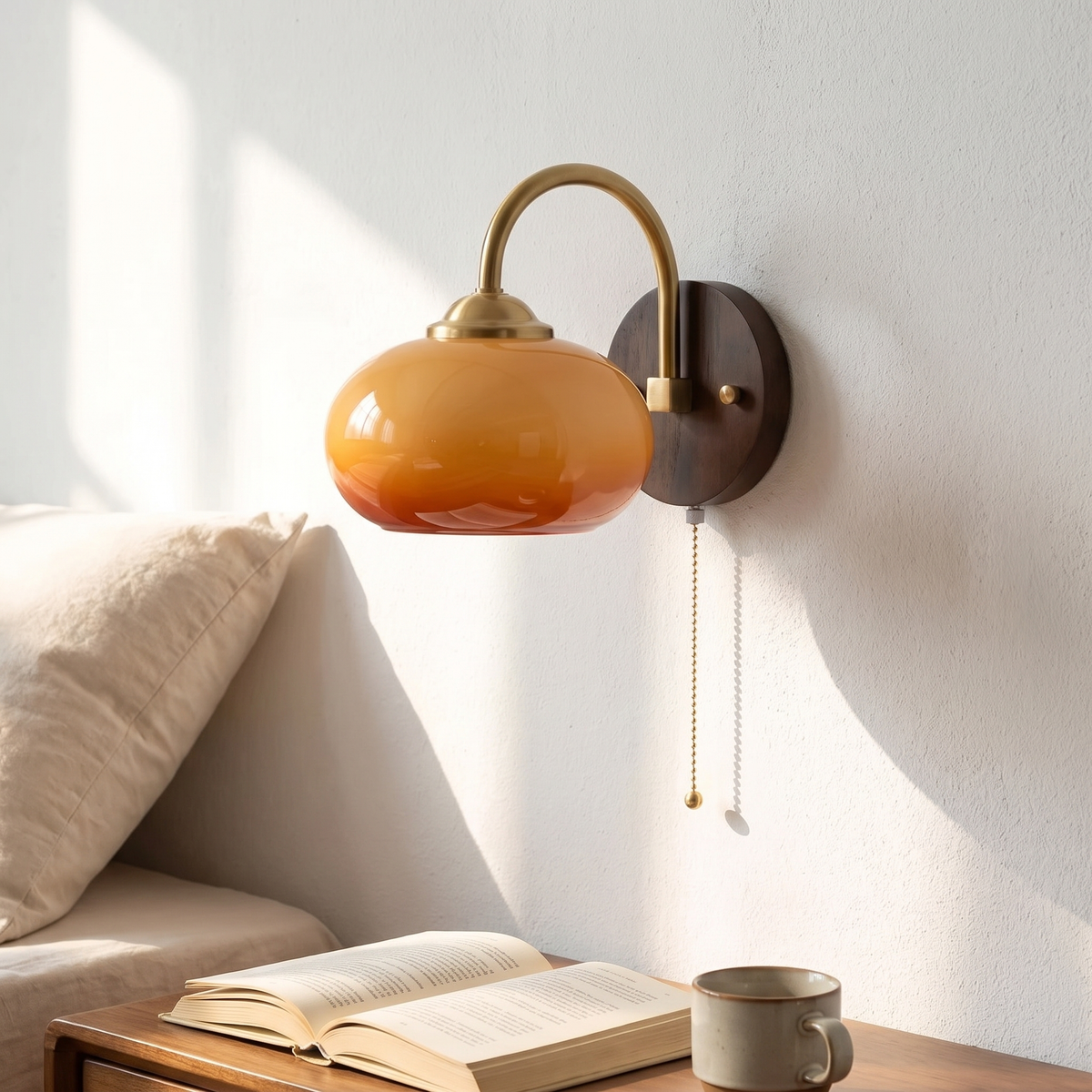 Stina wall sconce in Oval Caramel beside a bed above an open book and a cup