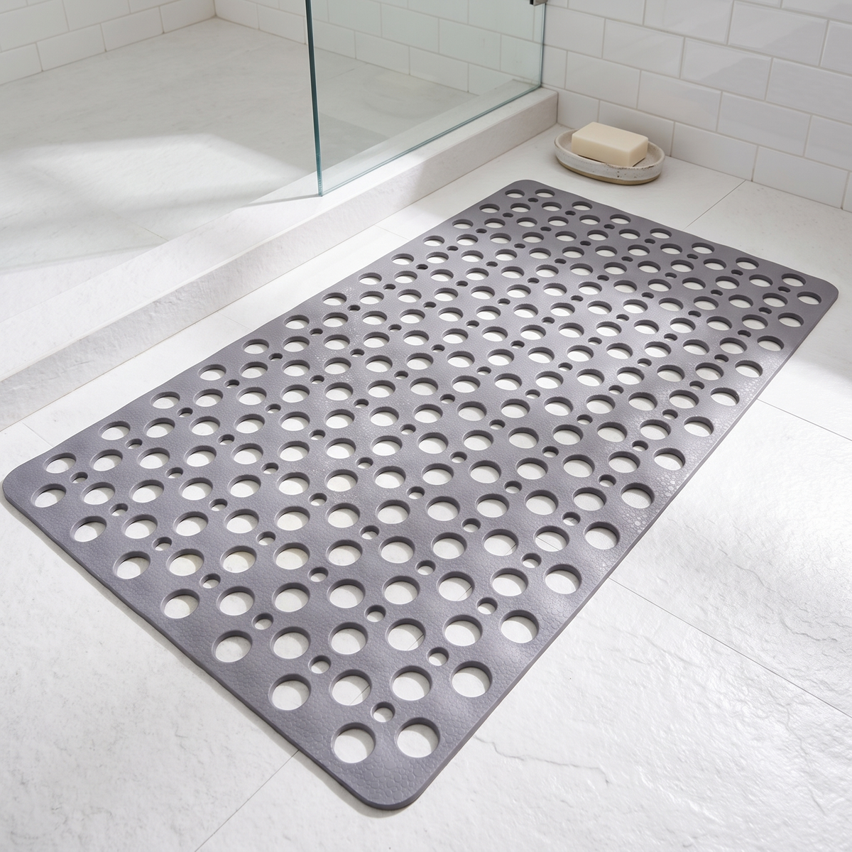 Gray suction cup shower mat with drain holes on a shower floor