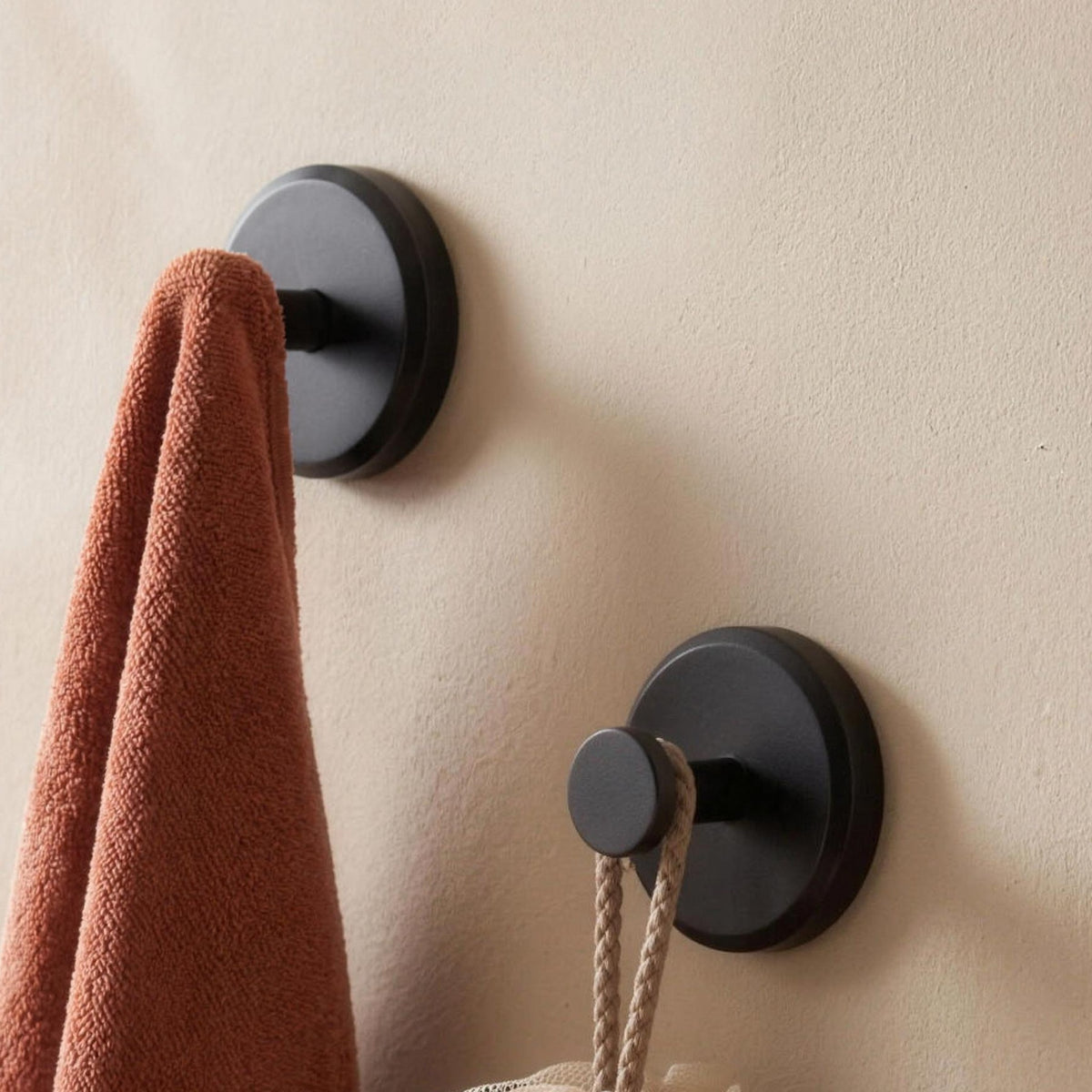 Two matte black suction wall hooks holding a towel and a bath sponge