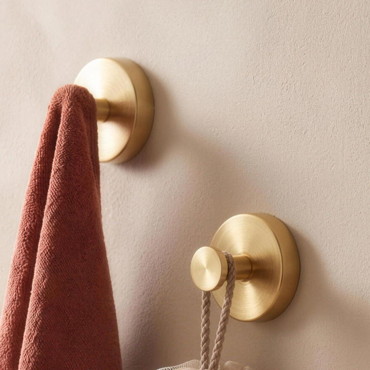 Two gold suction wall hooks holding a towel and a bath sponge