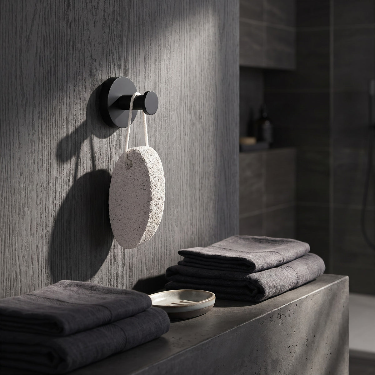 Matte black suction hook holding a pumice stone on a stone wall