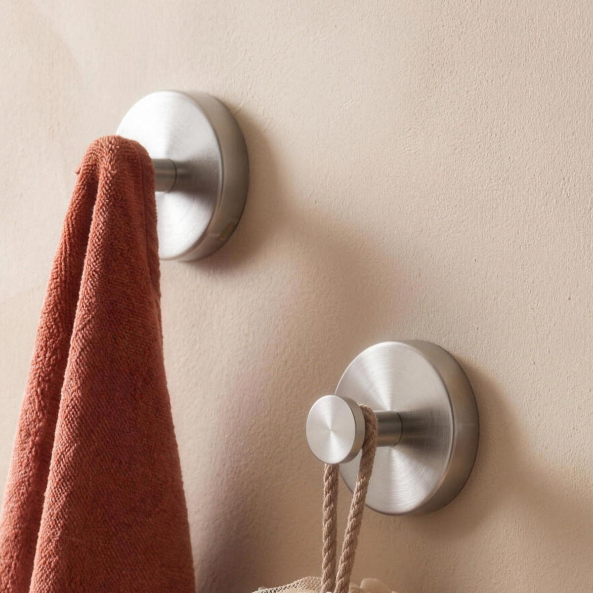 Two silver suction wall hooks holding a towel and a bath sponge