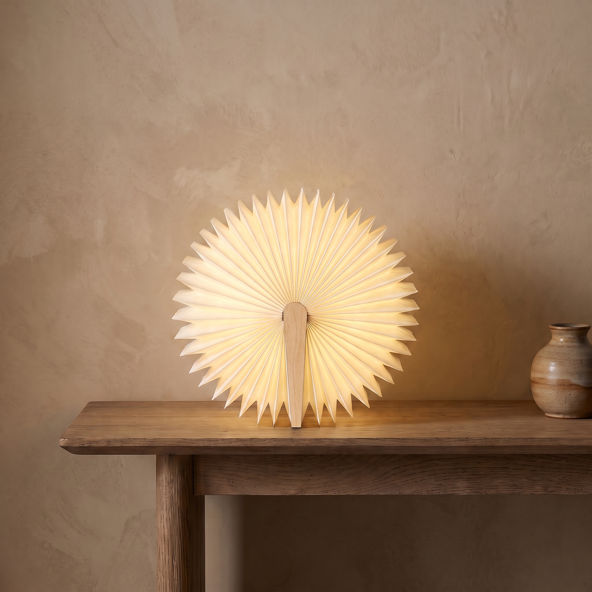 Sula book lamp with light wood covers, opened all the way round into a glowing lantern on an oak console