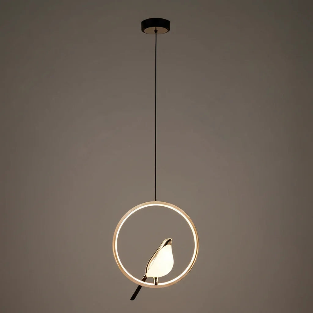 Gold ring frame bird pendant glowing against a taupe wall