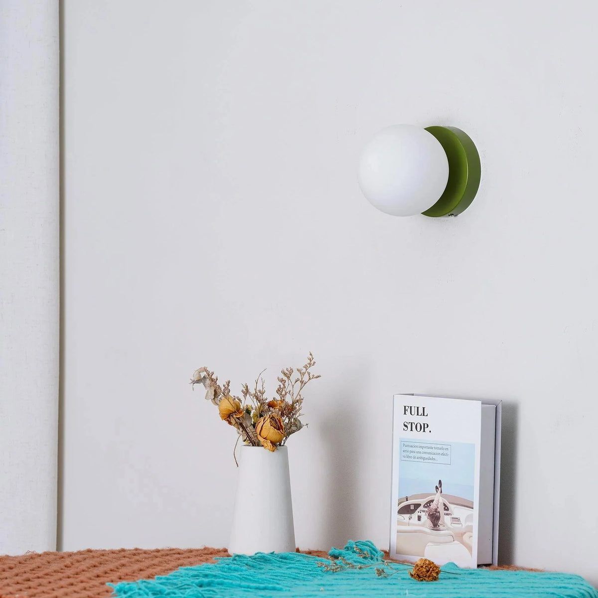 Ulla wall sconce in Green on a bedroom wall above a vase and a book