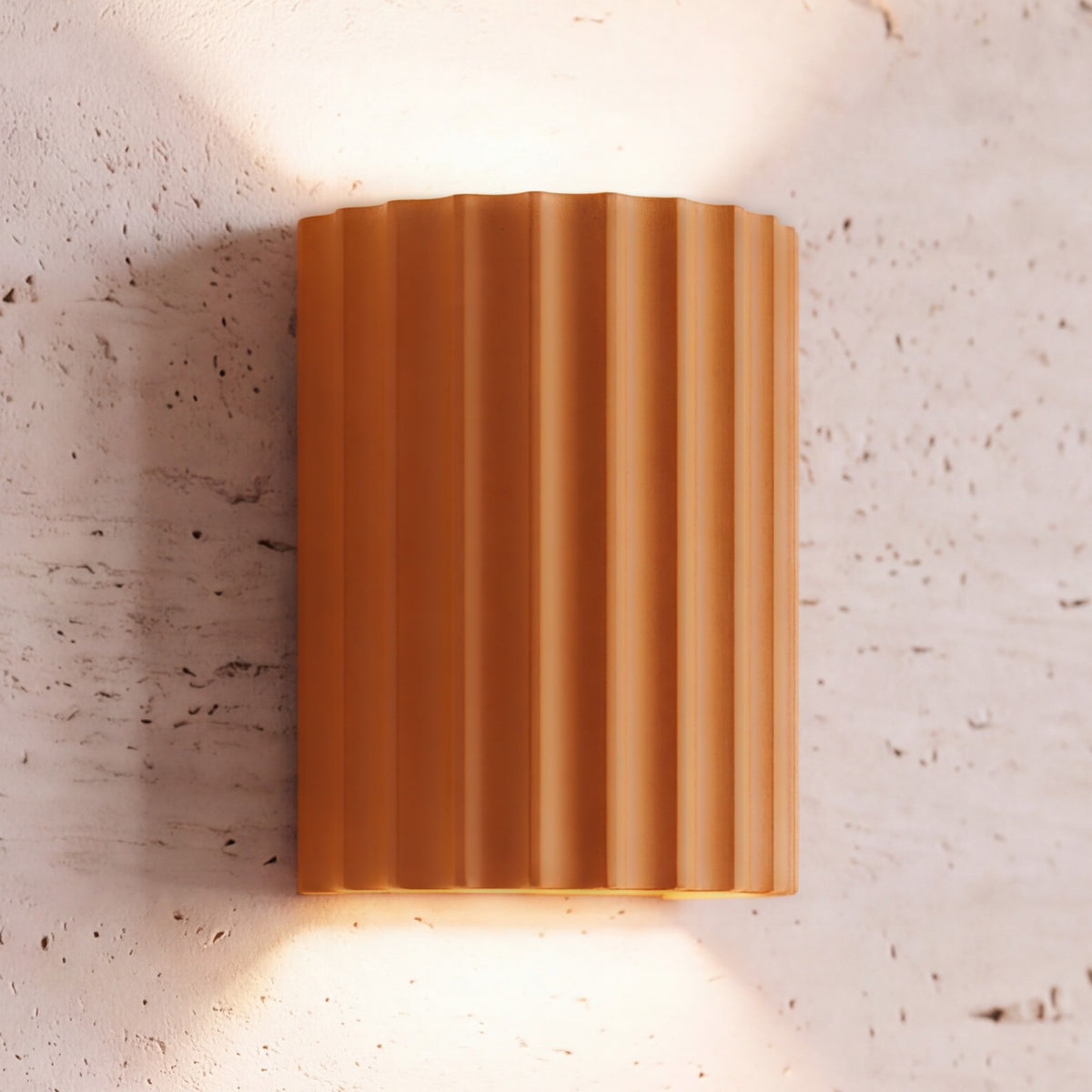 Unni LED wall sconce, orange fluted shell, lit up and down on a travertine wall